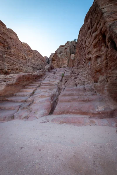 Stairs in the rock along Al Kubtha Trail (Indiana Jones Trail) leading to Al-Khazneh Treasury in the historic and archaeological city of Petra, Jordan against blue sky