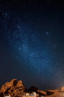 Gece gökyüzü yıldızlarla dolu ve Wadi Rum Çölü 'nün üzerindeki samanyolu kısmen köpük çadırı ve kayalık manzarayla dolu.