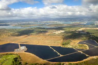 Hawaii adası Oahu 'nun güneş enerjisi tarlaları ve Waipahu ve Pearl City şehirlerinin arka planda mavi bulutlu gökyüzü manzarası.