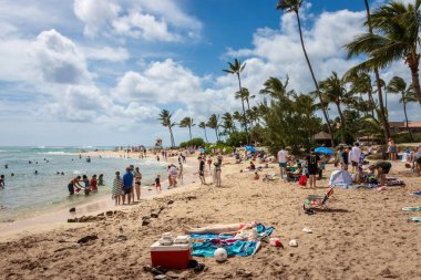 Koloa, ABD - 7 Nisan 2024: Kauai, Hawaii 'deki kalabalık Poipu Sahili' nde bulutlu mavi gökyüzüne karşı insanlar