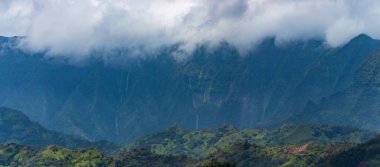 ABD 'nin Hawaii adası Kauai' nin kuzey kıyısında yükselen yemyeşil bitki örtüsüyle kaplı dağların manzarası bulutlu gökyüzüne karşı birkaç şelale ile