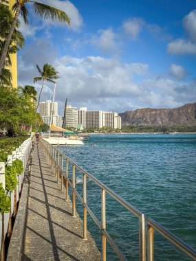 Waikiki Plajı Honolulu, Hawaii, ABD 'de sahil boyunca bulutlu mavi gökyüzüne karşı yürüyor