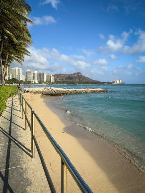 Waikiki Plajı Honolulu, Hawaii, ABD 'de sahil boyunca bulutlu mavi gökyüzüne karşı yürüyor