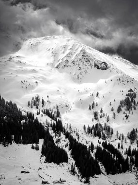 Avusturya Alplerinde Saalbach-Hinterglemm kayak bölgesindeki kar manzaralı dağ siyah beyaz bulutlu gökyüzüne karşı