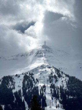 Elektrik hattı, Avusturya 'nın Saalbach-Hinterglemm kayak bölgesinde karla kaplı bir dağda dramatik bulutlu gökyüzüne karşı ilerliyor.