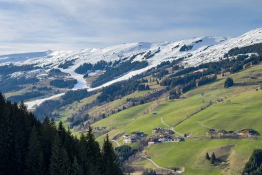 Scenic view of ski region of Saalbach-Hinterglemm with green meadows and slopes in bad conditions in the Austrian alps against blue sky with clouds in mid March 2024 clipart