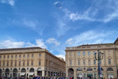 Torino, İtalya - 24 Nisan 2022: San Carlo Meydanı 'nda yayalar ve kabarcıklar bulutlu mavi gökyüzüne karşı