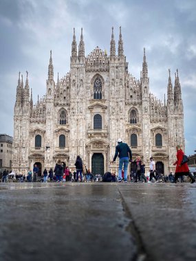 Milan, İtalya - 26 Nisan 2022: Milano Katedrali 'nin (Saint Mary' nin Doğuşu Metropolitan Katedrali - Basilikası) ve bulutlu gökyüzüne karşı tesadüfi insanlarla ön cephesi