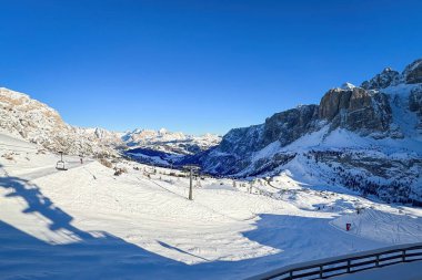 Scenic view from Gardena Pass to Kufar Alta Badia and mountains of the Fanes Group e.g. Cuntrines, Lagazuoi, Tofana di Rozes in winter against blue sky clipart