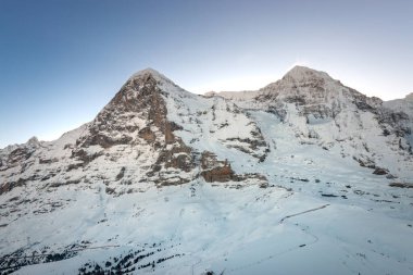 Sabahın erken saatlerinde İsviçre 'deki kar kaplı Eiger ve Mnch dağlarının mavi gökyüzüne karşı manzarası.