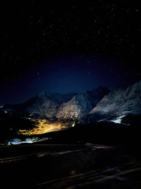 Panoramic view of illuminated Grindelwald at night seen from Maennlichen in winter against sky full of stars clipart