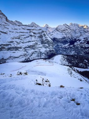 Panoramic view of upper Lauberhorn Ski World Cup race course against snowcapped mountains in Wengen, Switzerland on a beautiful morning with blue sky clipart