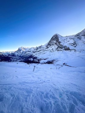 İsviçre 'deki ünlü kar örtüsü Eiger Dağı' nın panoramik manzarası Grindelwald ve Wetterhorn (kışın en solunda) ile mavi gökyüzüne karşı
