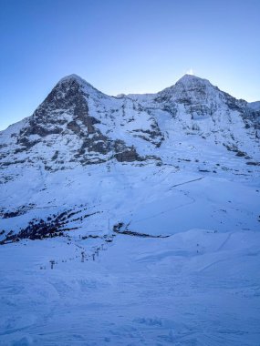 Scenic view of snowcovered Eiger and Moench mountains in Switzerland early in the morning against blue sky clipart