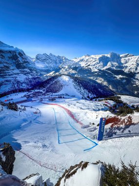 Wengen, Switzerland - January 13, 2024: Scenic view of legendary Hundschopf jump at Lauberhorn downhill ski alpin race course against blue sky. clipart