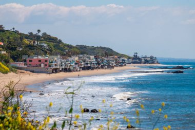Corral Beach 'in manzarası ve deniz kenarındaki cambaz evleri, Malibu, California, ABD' de Nisan 2024 'te bulutlu mavi gökyüzüne karşı