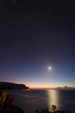 Hawaii 'nin Kauai adasının kuzey kıyısının gece vakti ünlü Napali kıyılarıyla ay ve yıldızlı mavi gökyüzüne karşı manzarası.