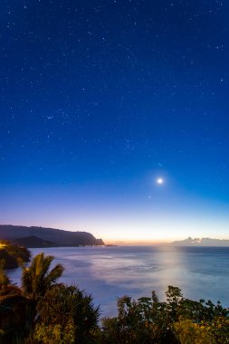 Hawaii 'nin Kauai adasının kuzey kıyısının gece vakti ünlü Napali kıyılarıyla ay ve yıldızlı mavi gökyüzüne karşı manzarası.