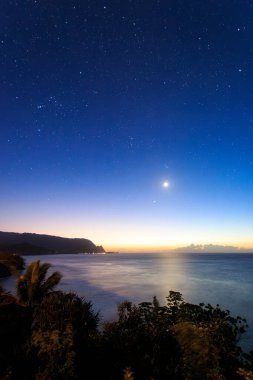 Hawaii 'nin Kauai adasının kuzey kıyısının gece vakti ünlü Napali kıyılarıyla ay ve yıldızlı mavi gökyüzüne karşı manzarası.