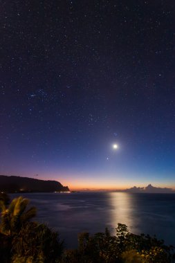 Hawaii 'nin Kauai adasının kuzey kıyısının gece vakti ünlü Napali kıyılarıyla ay ve yıldızlı mavi gökyüzüne karşı manzarası.