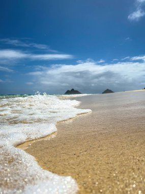 Kailua, Oahu, Hawaii, ABD 'deki ünlü Lanikai Sahili' nde, arka planda mavi bulutlu Mokulua Adası ile birlikte bir dalga.