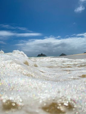 Kailua, Oahu, Hawaii, ABD 'deki ünlü Lanikai Sahili' nde, arka planda mavi bulutlu Mokulua Adası ile birlikte bir dalga.