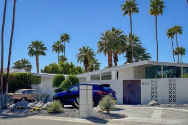 Palm Springs, California, USA - April 16, 2024: Example of mid-century modern architecture home 815 Camino Sur with cars and palm trees against blue sky