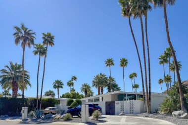 Palm Springs, California, USA - April 16, 2024: Example of mid-century modern architecture home 815 Camino Sur with cars and palm trees against blue sky