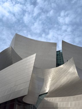 Los Angeles, Kaliforniya, ABD - 18 Nisan 2024: Walt Disney Konser Salonu 'nun kıvrımlı paslanmaz çelik cephesi bulutlu mavi gökyüzüne karşı