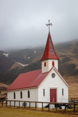 Vikurkirkja olarak da bilinen Vik i Myrdal Kilisesi, İzlanda 'da bulutlu bir gökyüzünün altında yuvarlanan tepelere karşı kırmızı çatısı ve çan kulesiyle ayakta duruyor.