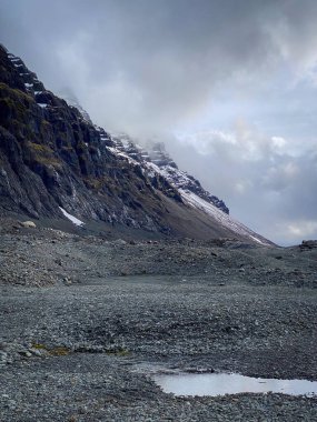 İzlanda 'nın güneyinde katmanlı kaya ve kar ile dik yamaçlar alçak bulutlara yükselir.