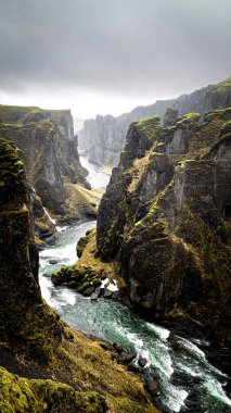 Fjadrargljufur vadisinin dik yosunlu duvarları Güney İzlanda 'daki kıvrımlı Fjadra nehrinin çerçevesini yumuşak gri bir gökyüzünün altında yapar.