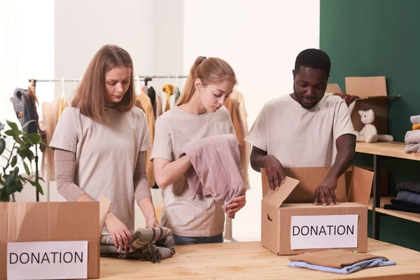 Группа Трех Волонтеров Работающих Вместе Благотворительной Организации Сортировки Упаковки Одежды — стоковое фото