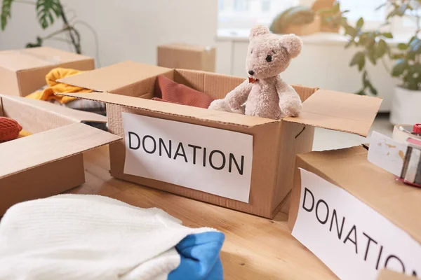 No people shot of cardboard donation boxes with clothes and toys on table in charity organization room