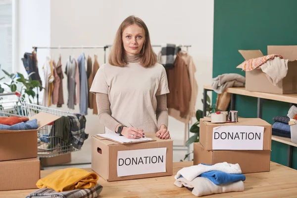 Portrait of modern mature Caucasian woman volunteering in clothes donation charity looking at camera