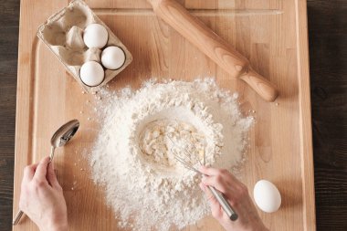 Tanınmayan bir kadının, un ve yumurtayı ahşap tahtada çırpıyla merdaneyle karıştırması.