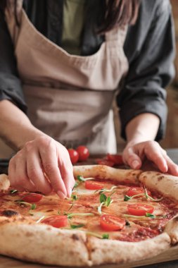 Önlüklü, tanınmayan bir kadının, pizzanın üzerine domatesli bezelye yaprağı koyarken aile için hazırladığı yakın plan.