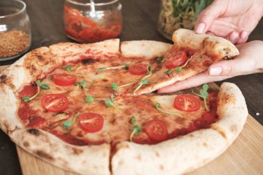 Tanınmayan bir kadının, tahta tahtadan bezelye yaprakları ve domateslerle süslenmiş sebzeli pizzayı aldığı yakın plan.