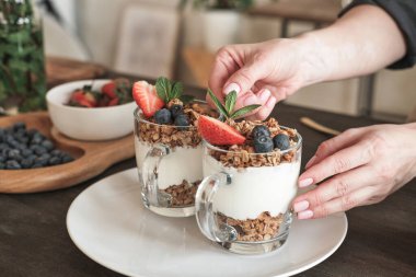 Mutfakta meyvelerle granola süslerken tanınmayan bir kadının yaprağı ayarladığı yakın plan.