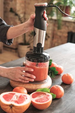 Mutfak tezgahında dikilip greyfurtu mutfak blendırına öğüten tanınmamış bir kadının yakın çekimi.