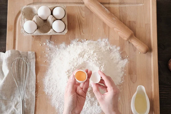 stock image Above view of unrecognizable woman separating yolk from egg white using shell above wooden board with flour