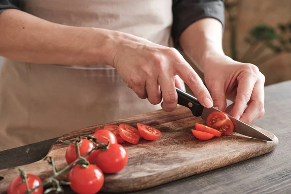 stock image Close-up of female hands slicing cherry tomato with knife on wooden board, cooking vegetable salad