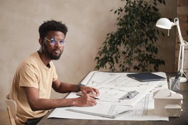 Ofiste planları olan yuvarlak gözlüklü yaratıcı Afro-Amerikan mimarın portresi.