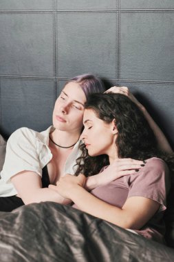 Çekici bir genç kadın yatakta uzanmış esmer kız arkadaşını kucaklıyor.