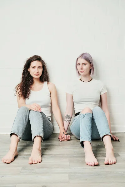 Retrato Contenido Joven Lesbianas Caucásicas Jeans Sentados Suelo Tomados Mano — Foto de Stock