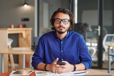 Gözlüklü ciddi bir melez iş adamının portresi. Ofisteki kağıtlarla dolu masada oturuyor.