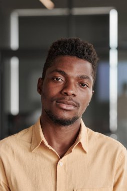 Modern ofiste sakallı, sarı gömlekli, sakin, genç siyahi bir müdürün portresi.