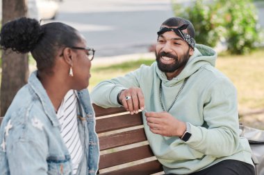 Kapüşonlu yakışıklı sakallı adam bankta oturuyor ve şehirdeki siyah kıza komik bir hikaye anlatıyor.