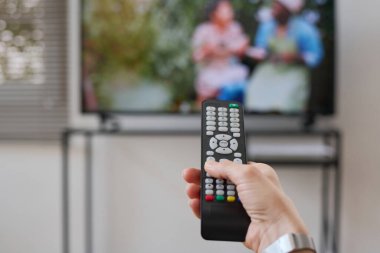 Evde boş zamanlarında TV 'de uzaktan kumandayla kanal değiştiren bir kadının yakın çekimi.