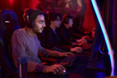Kulaklıklı bir grup konsantre genç oyuncu sırada oturup eSport turnuvasına katılıyor.